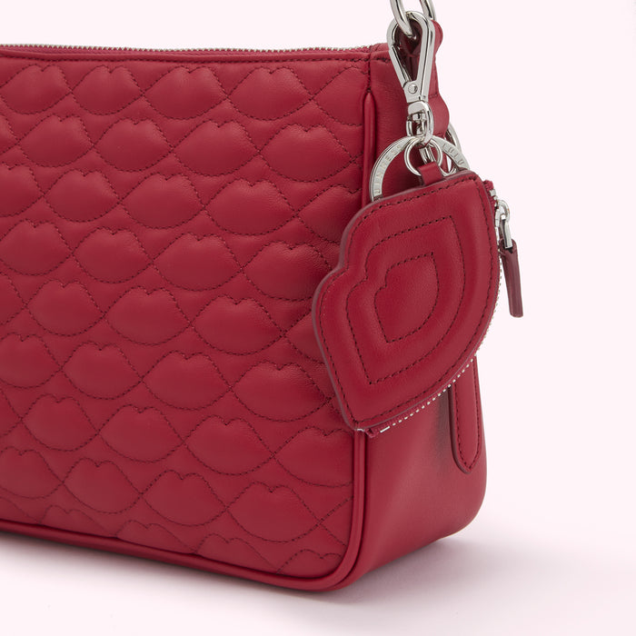 Close-up of a red quilted crossbody bag with a lip-shaped zipper pull and charm.