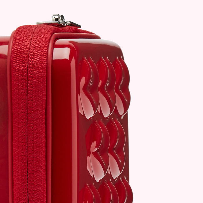 Close-up of a red, glossy cosmetic case with heart-shaped embossing and a red zipper.