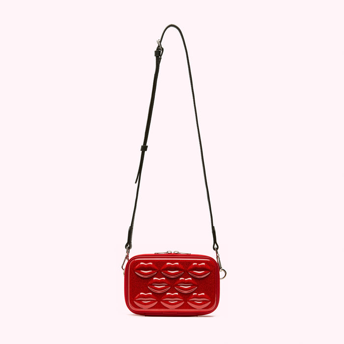 Red crossbody bag with lip-shaped embellishments and a black strap against a white background.