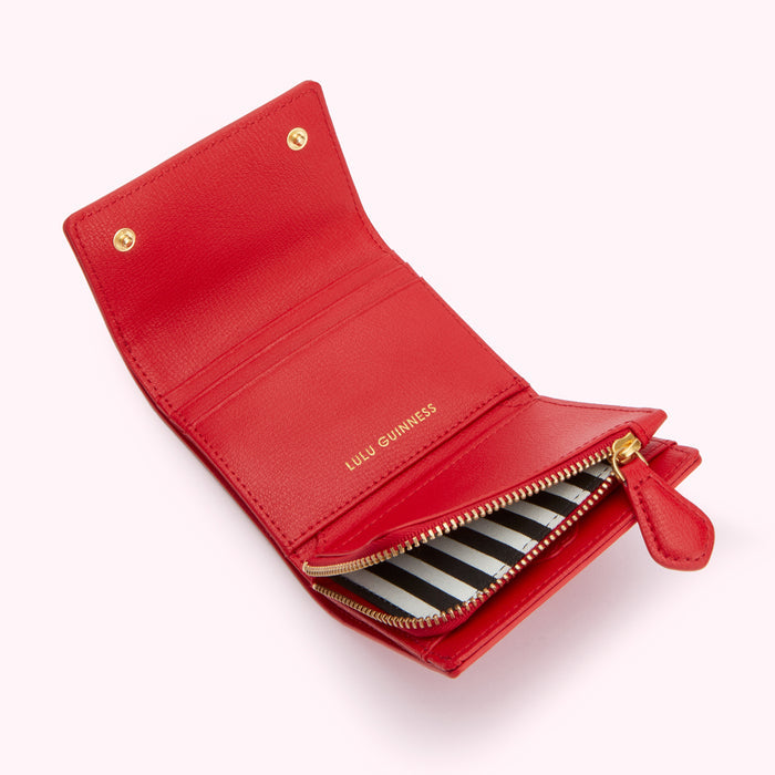 Open red leather Lulu Guinness wallet with a black and white striped zipper.