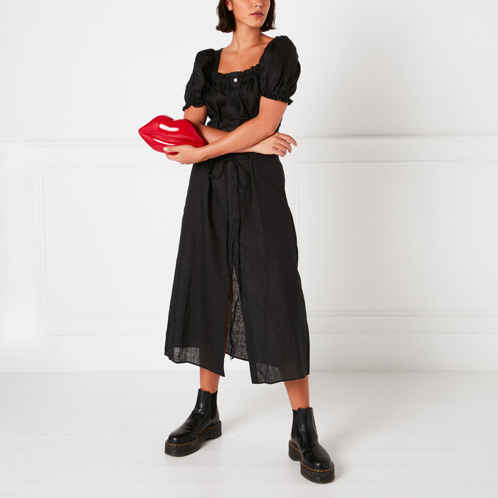 A model in a black dress holds a red lip-shaped clutch against a white background.