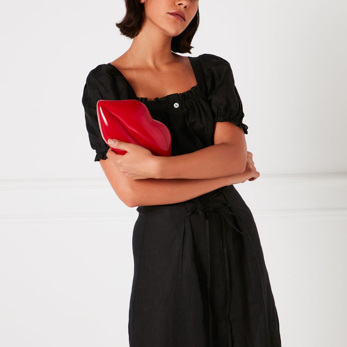 Woman in black dress holding a red lip-shaped clutch against a white background.