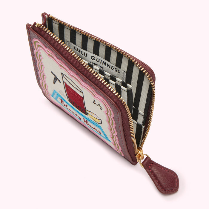 Burgundy Lulu Guinness zip-around purse with an embroidered illustration of a drink and the words "Bloody Mary" on the front; the interior lining is black and white striped.