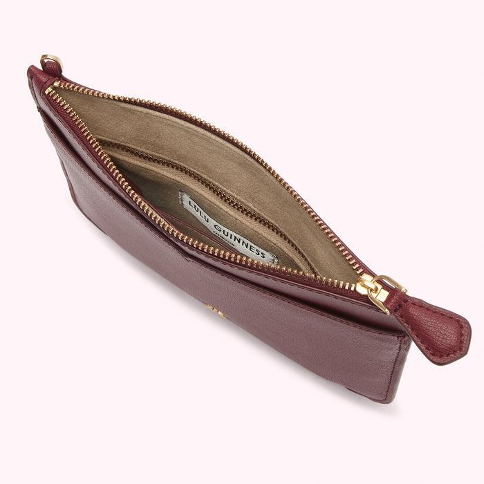 Burgundy leather Lulu Guinness zip-around pouch open to reveal a beige interior with multiple compartments.