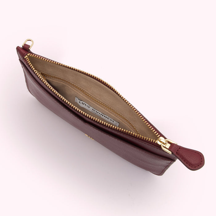 A burgundy Lulu Guinness zip-around pouch is shown open, revealing a beige interior with a brand label.