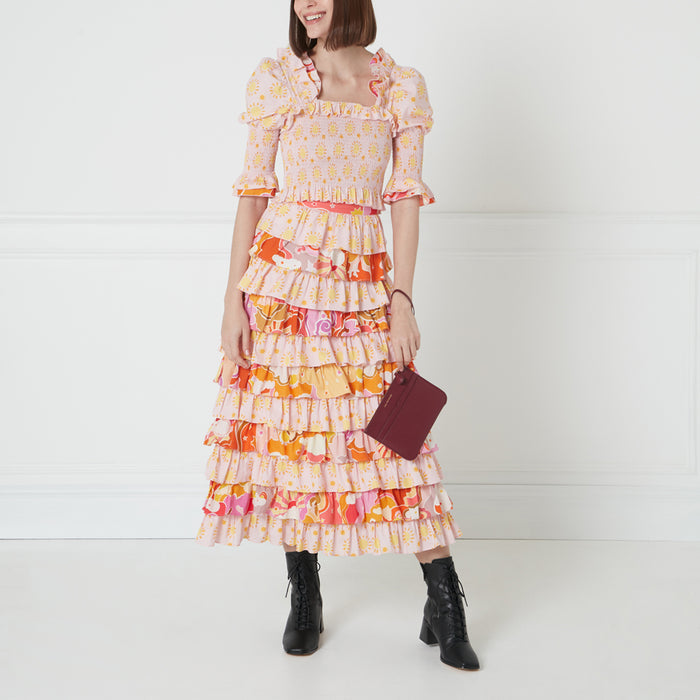 Woman in a pink and orange tiered midi dress and burgundy purse against a white background.