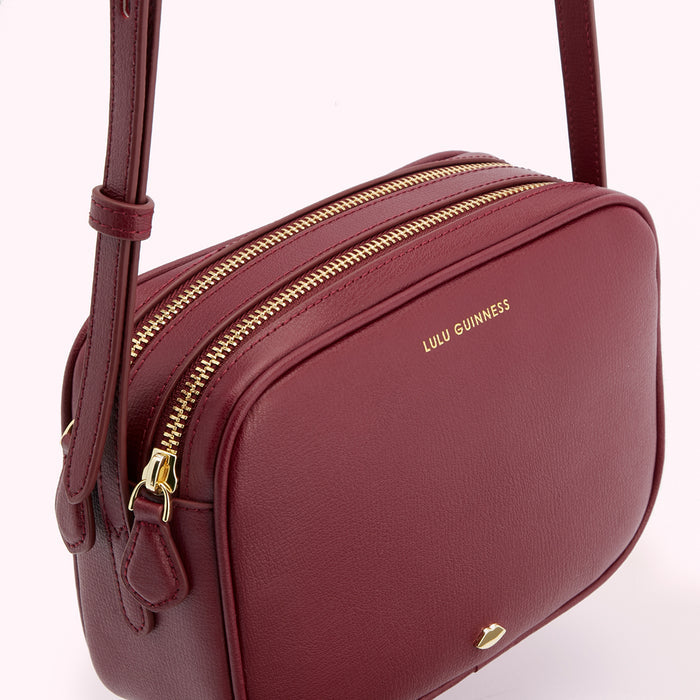Close-up of a burgundy Lulu Guinness crossbody bag with gold zippers.