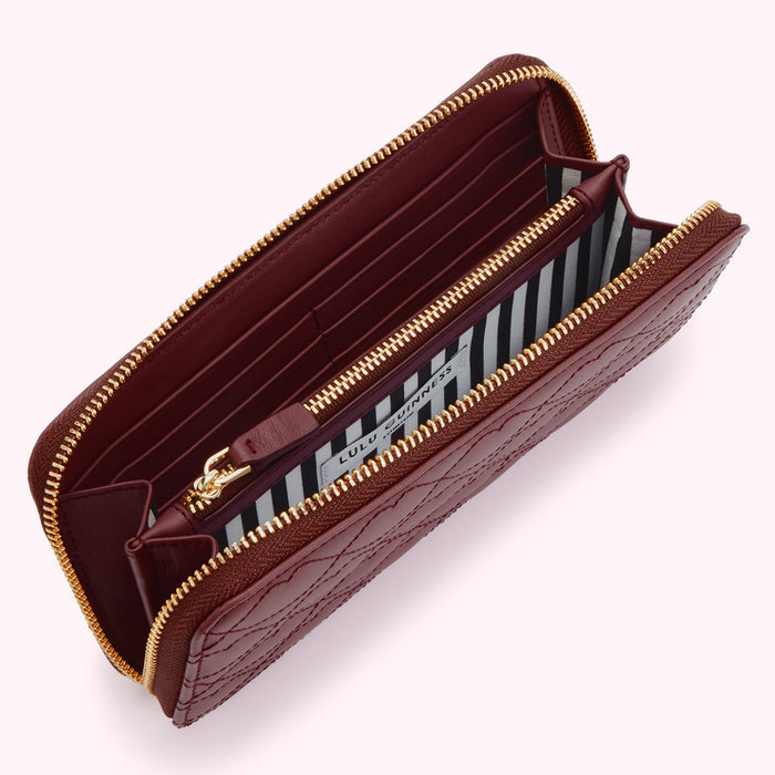 Open burgundy quilted zip-around wallet with gold zippers and black and white striped interior lining.