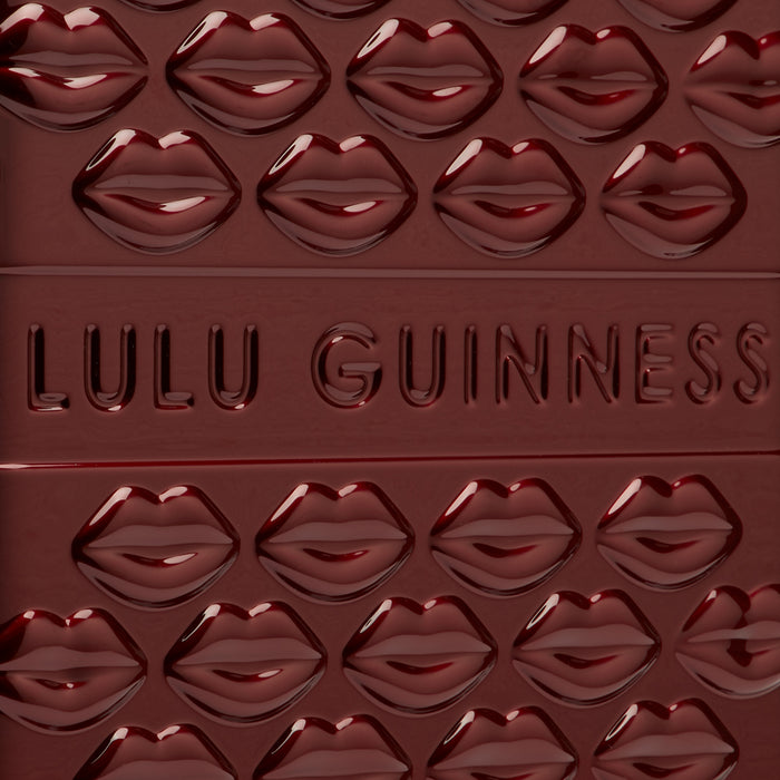 Close-up of a dark red Lulu Guinness compact with a repeating embossed lip pattern and the brand name embossed in the centre.