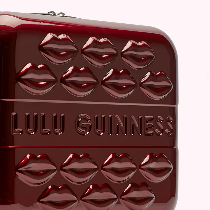 Close-up of a dark red Lulu Guinness suitcase adorned with embossed lips and the brand name.