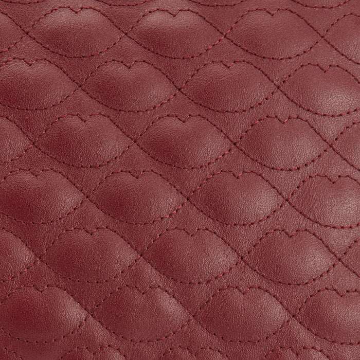 Close-up of a quilted burgundy leather texture with lip-shaped stitching.