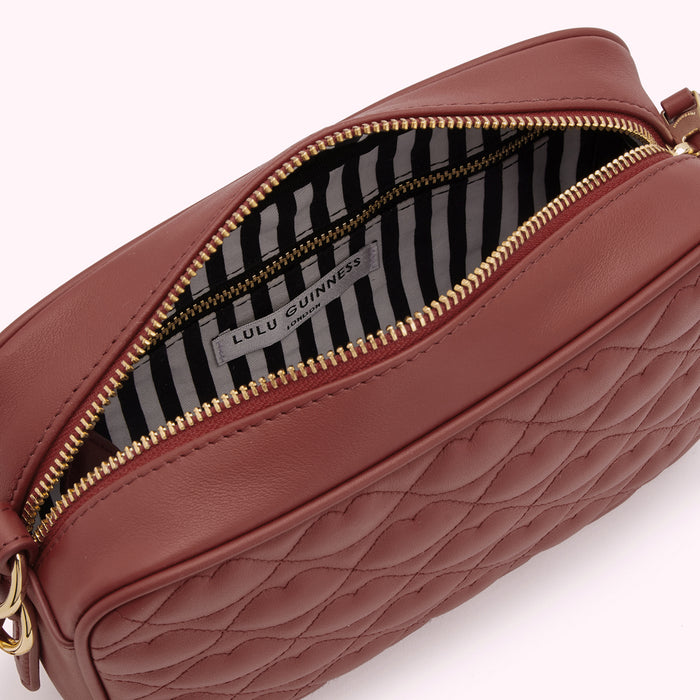 Inside of a dusty rose quilted heart-shaped Lulu Guinness crossbody bag. The interior lining is black and white striped.