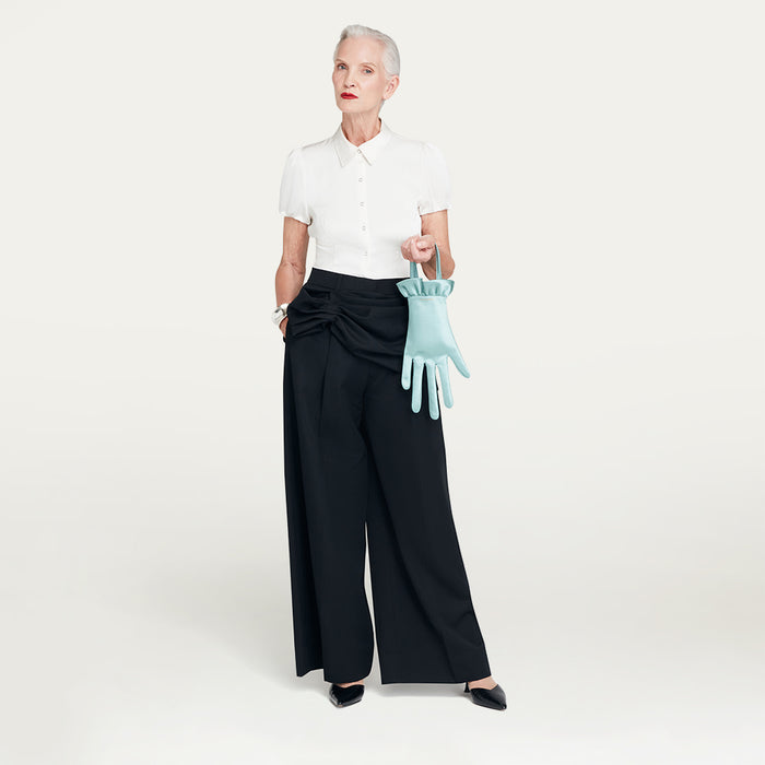 Woman holding a light blue glove shaped handbag against a white background