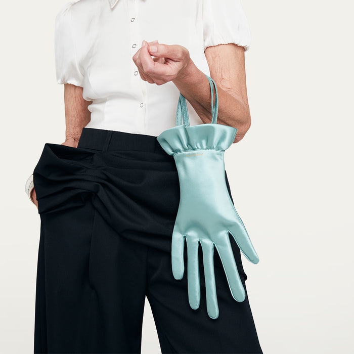 Person holding a light blue glove shaped handbag against a plain background
