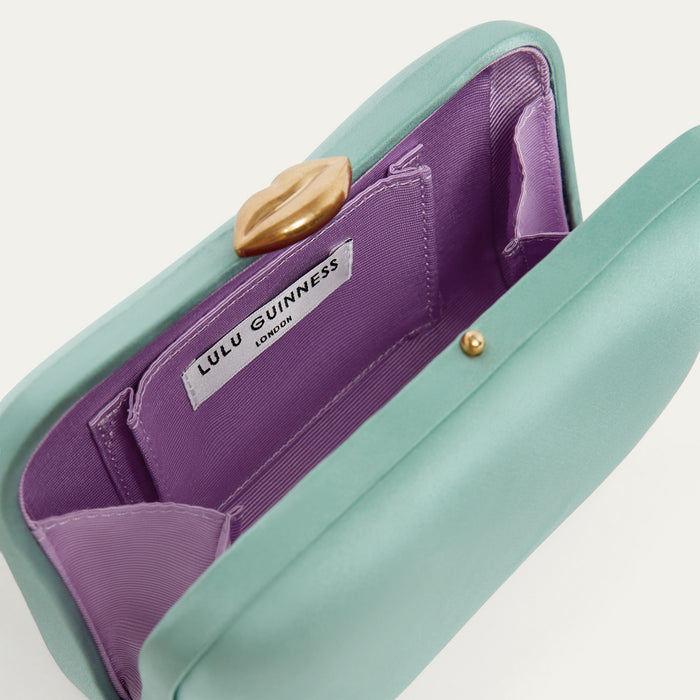 Mint green handbag with a gold lip-shaped claps, purple interior and Lulu Guinness label on a white background