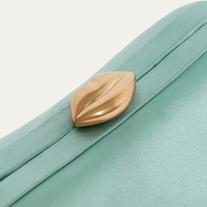 Teal satin clutch bag with a gold lip-shaped clasp on a light gray background