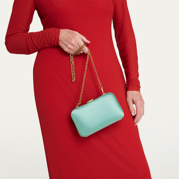 Person wearing a red dress holding a turquoise satin handbag with a gold chain.