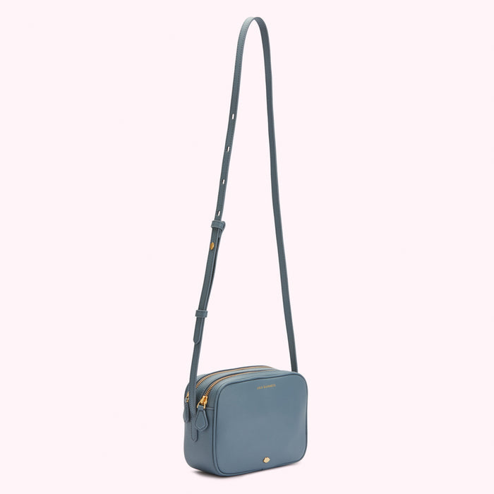 A dusty blue crossbody bag with gold hardware and a long strap.