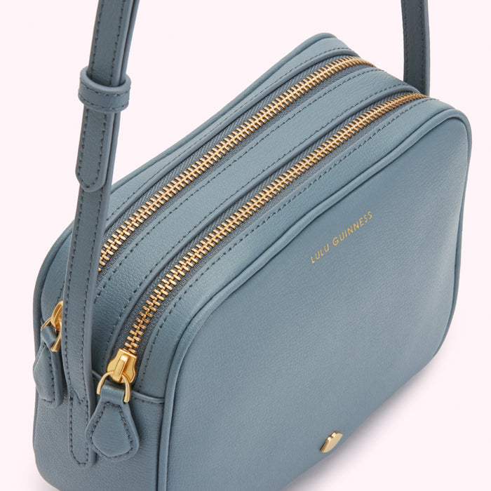 Dusty blue Lulu Guinness crossbody bag with gold zippers.