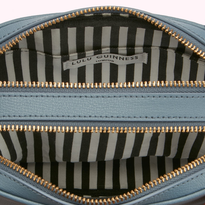 Close-up of the inside of a light blue Lulu Guinness London handbag, showing the black and white striped lining and gold zippers.