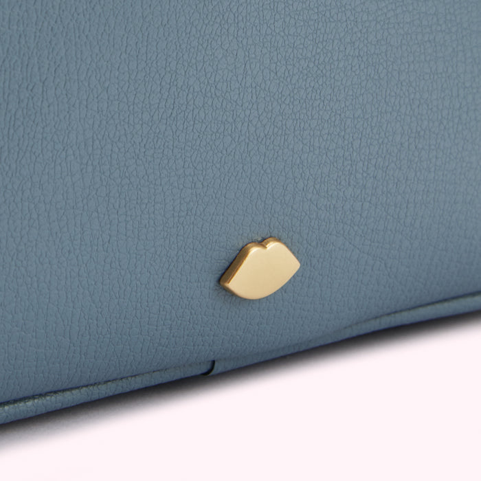 Close-up of a dusty blue textured leather purse with a gold lip-shaped emblem.