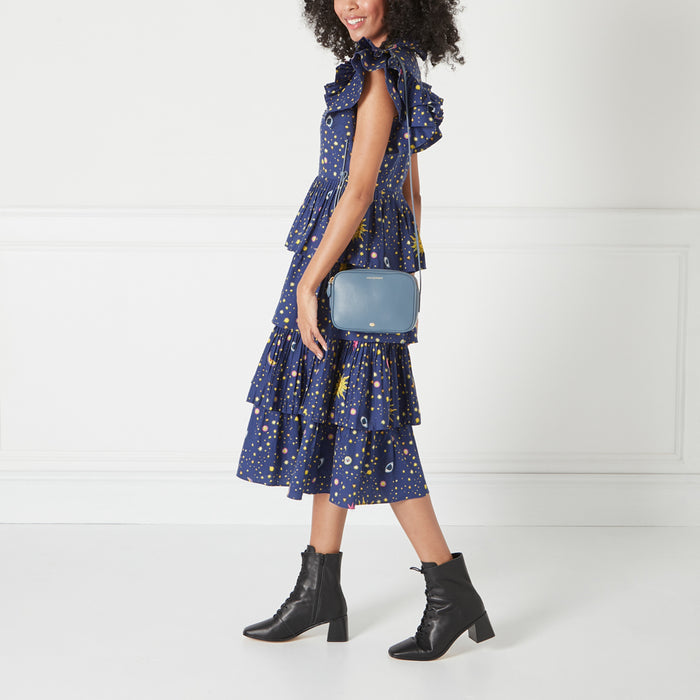 A woman wearing a navy dress with a celestial print carries a light blue crossbody bag.