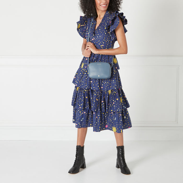 A woman in a navy blue dress with a celestial print carries a small, rectangular blue crossbody bag.