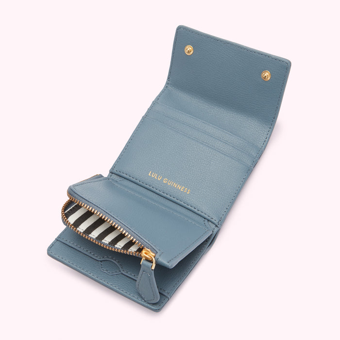 A dusty blue Lulu Guinness leather wallet open to reveal a black and white striped zipper.