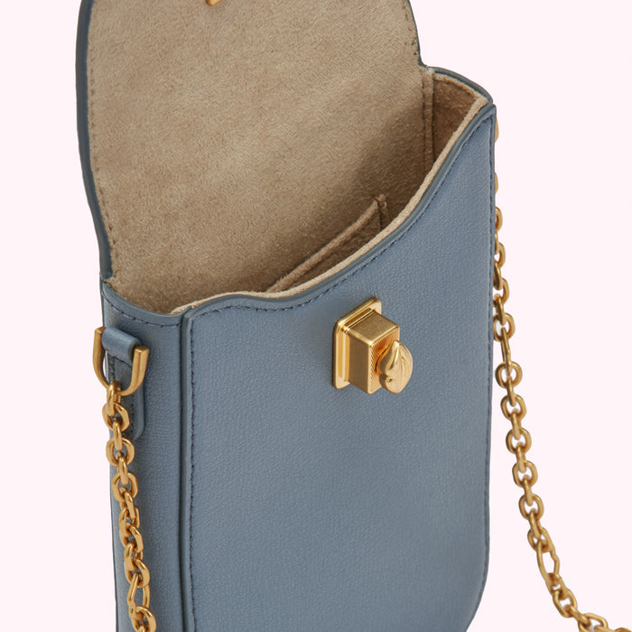 Close-up of a dusty blue leather crossbody bag with gold chain strap and clasp. The bag is open, revealing a light beige interior.