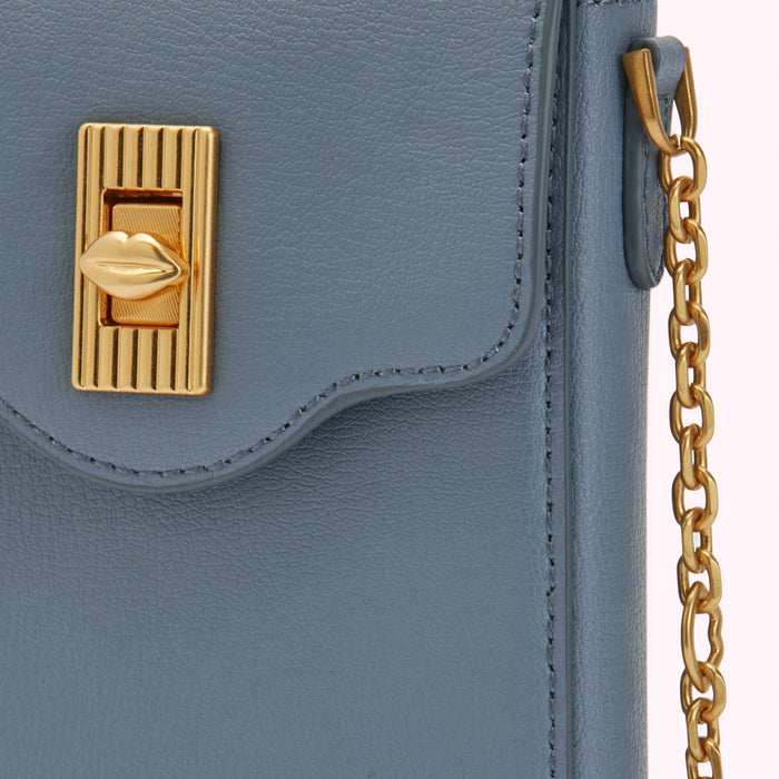 Close-up of a blue leather handbag with a gold lip-shaped clasp and gold chain strap.