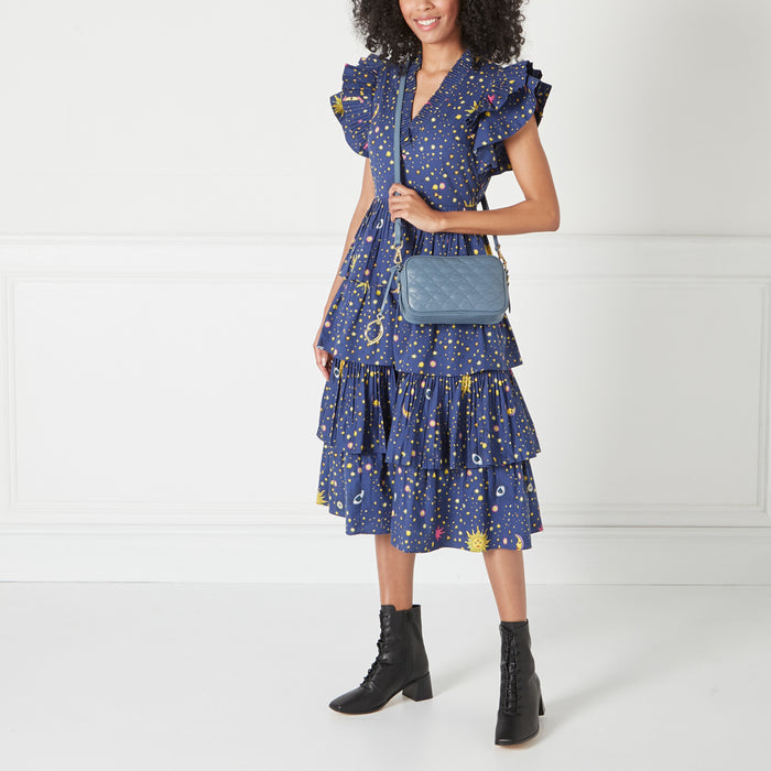 Woman in a blue dress and black boots carrying a blue quilted crossbody bag.