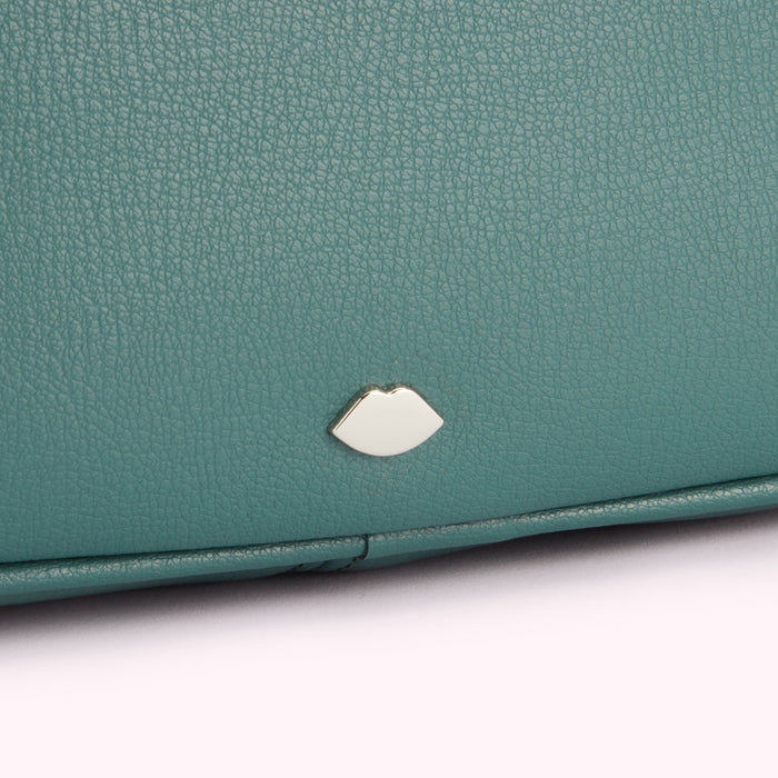Close-up of teal textured leather with a silver lip-shaped emblem.