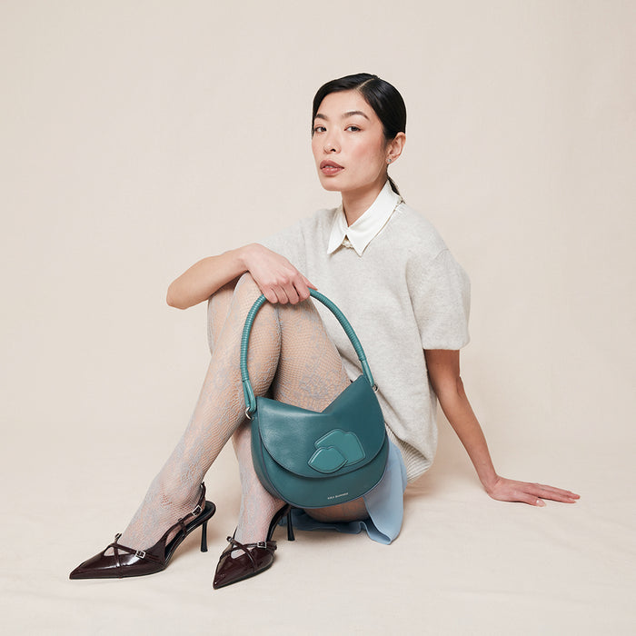 Woman holding a teal leather handbag with a lip design on the front against a plain background