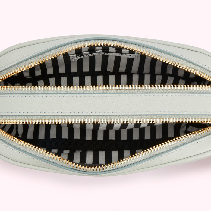 Interior of a light blue crossbody bag with gold zippers and a black and white striped lining.