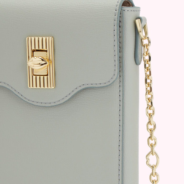 Close-up of a light grey leather handbag with a gold lip-shaped clasp and gold chain strap.