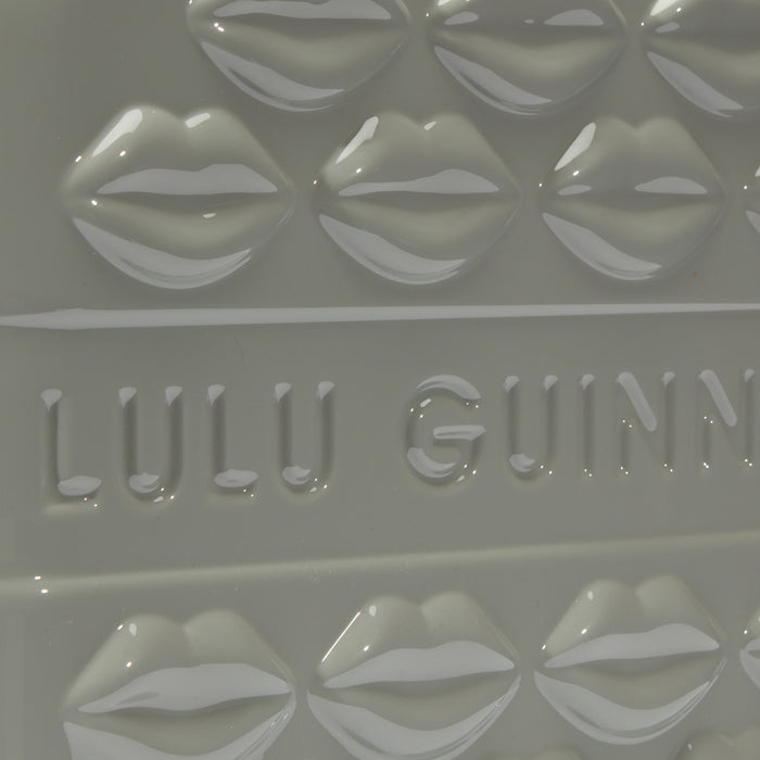 Close-up of a pale grey Lulu Guinness item featuring a repeating pattern of embossed lips and the brand name.