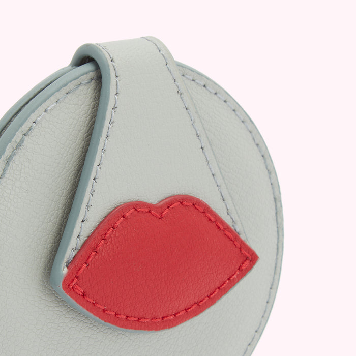 Close-up of a light grey leather compact mirror with a red leather lip design.