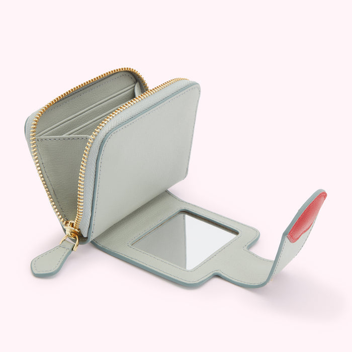A light teal compact wallet with a gold zipper and a small mirror is open, showcasing its interior and a red detail.