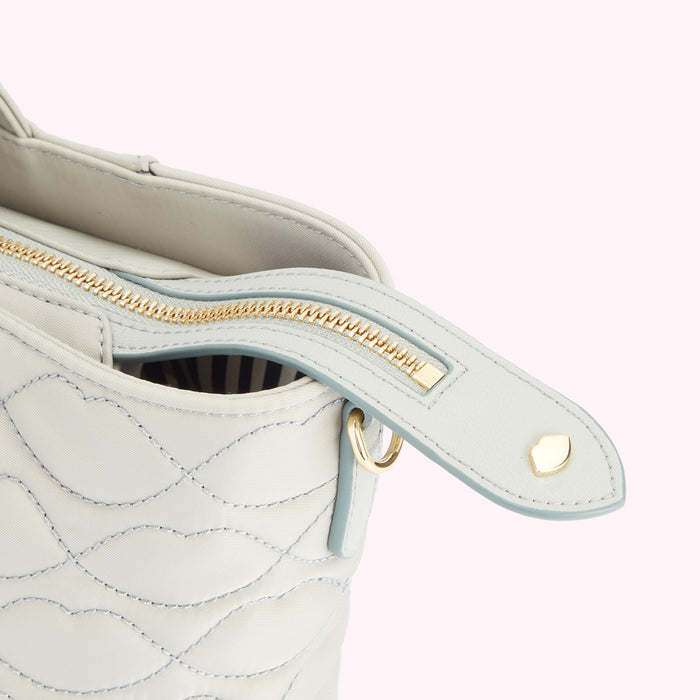 Close-up of a light grey quilted handbag's zipper and top flap, showcasing its details and light blue accents against a pink background.