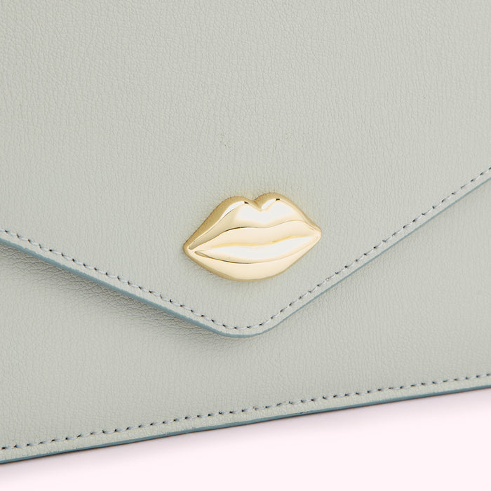 Close-up of a light sage green leather wallet with a gold lip-shaped clasp.