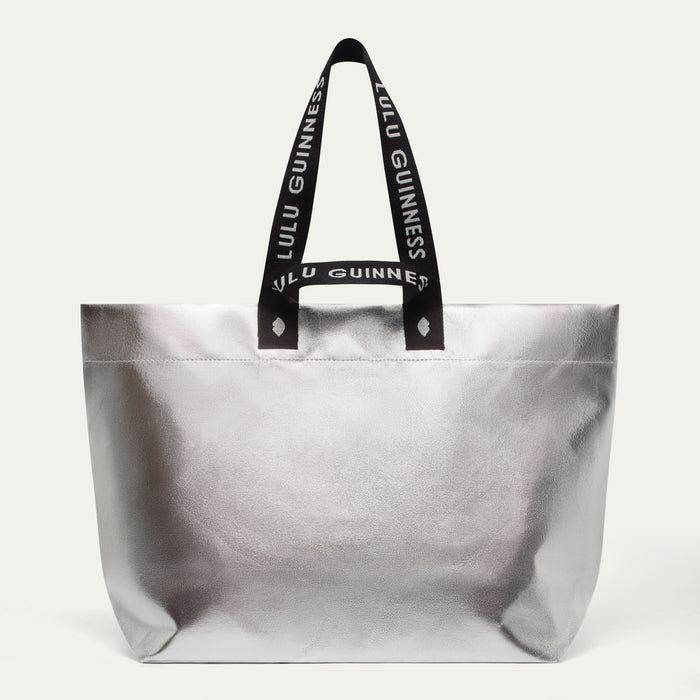 Silver tote bag with black handles featuring 'Lulu Guinness' branding on a white background.
