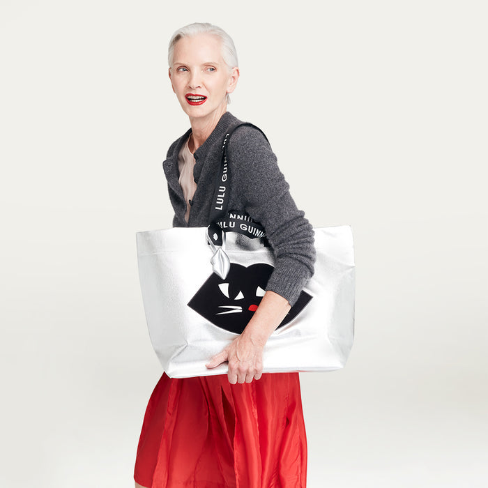 Woman holding a silver tote bag with a cat design on a gray background