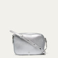 Silver crossbody bag with a lip shaped metal pin on a light gray background