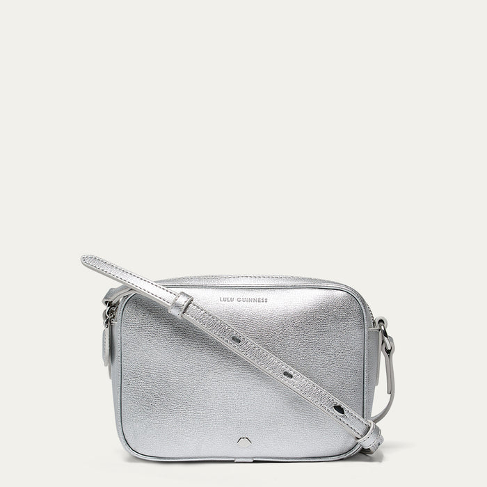 Silver crossbody bag with a lip shaped metal pin on a light gray background
