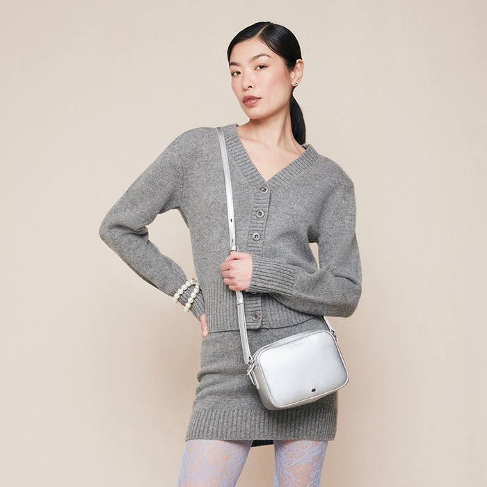 Woman wearing a gray knit dress holding a silver handbag against a beige background