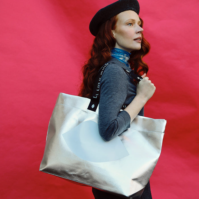 Woman holding a silver tote bag with a red background