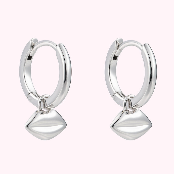 Angled image of a pair or sterling silver hoop earrings with lip charms.