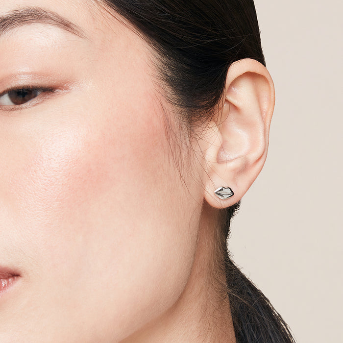 Close-up of a person wearing a silver lip-shaped stud earring on a neutral background