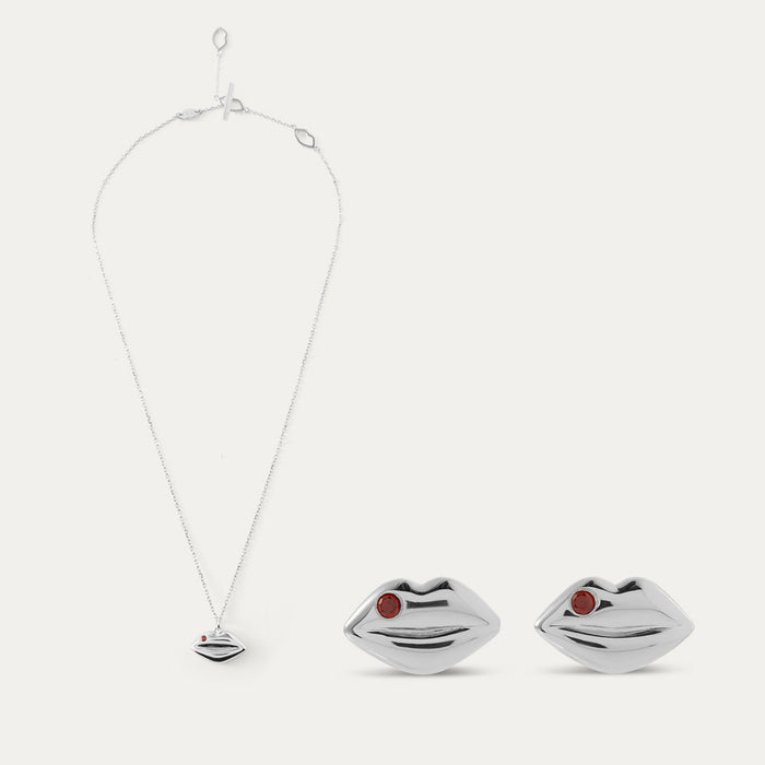 Silver lip-shaped pendant and stud earrings with red stones on a white background
