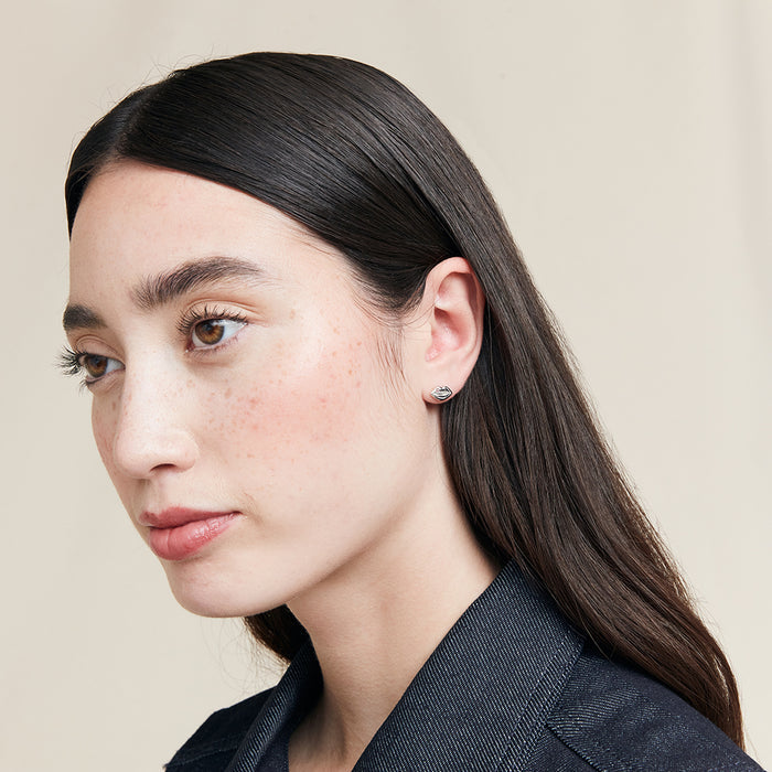 Close-up of a person with long dark hair wearing a silver lip shaped stud earring against a beige background